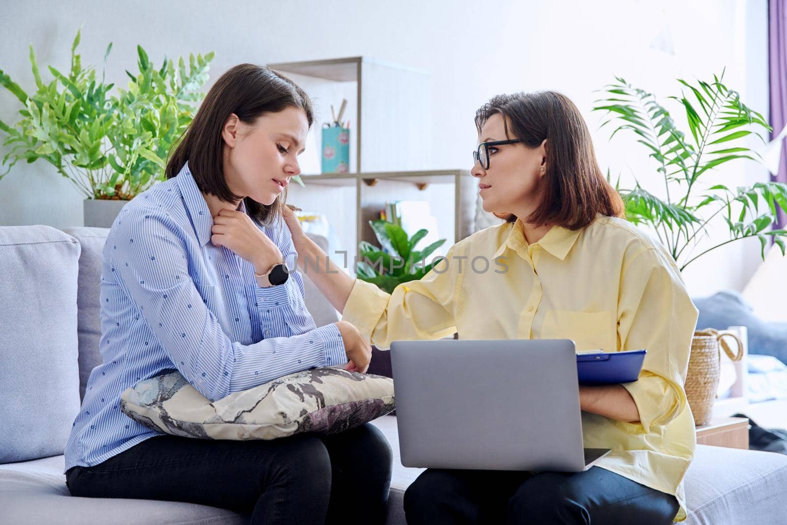 Upset sad young woman at session with psychologist. Mature female psychologist counseling helping patient, women sitting on couch in office. Psychology, psychiatry, treatment, mental health concept