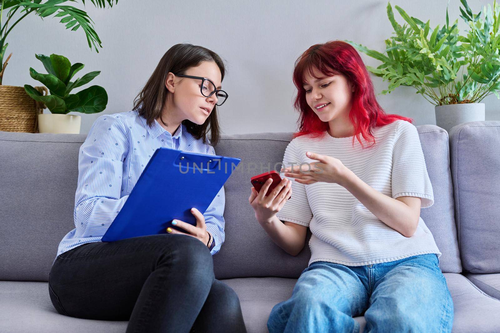 Psychologist counseling teenage female, individual therapy in doctors office. Professional counselor helping teenager, girl with smartphone. Mental health, adolescence, psychology, psychiatry concept