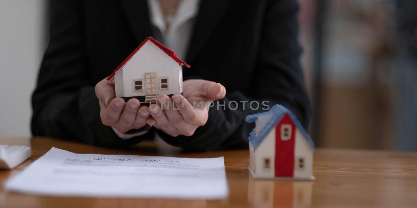 Home protection concept, close up of female hands sheltering modern house.