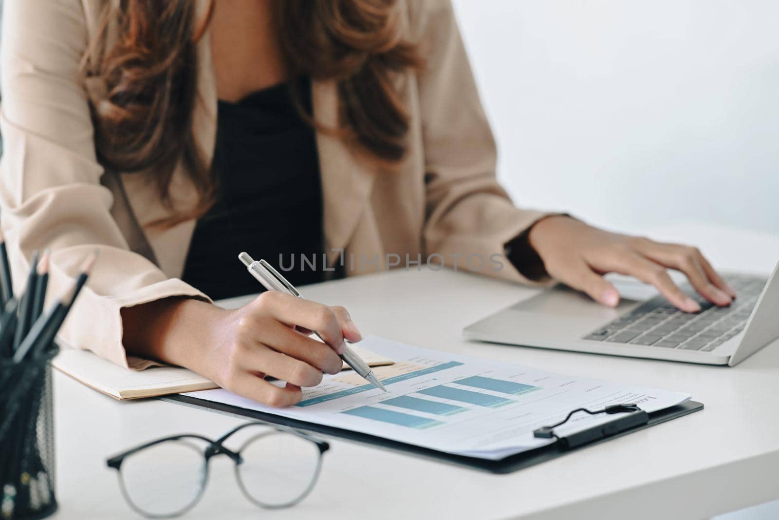 Businesswoman typing on laptop and writing information on document.