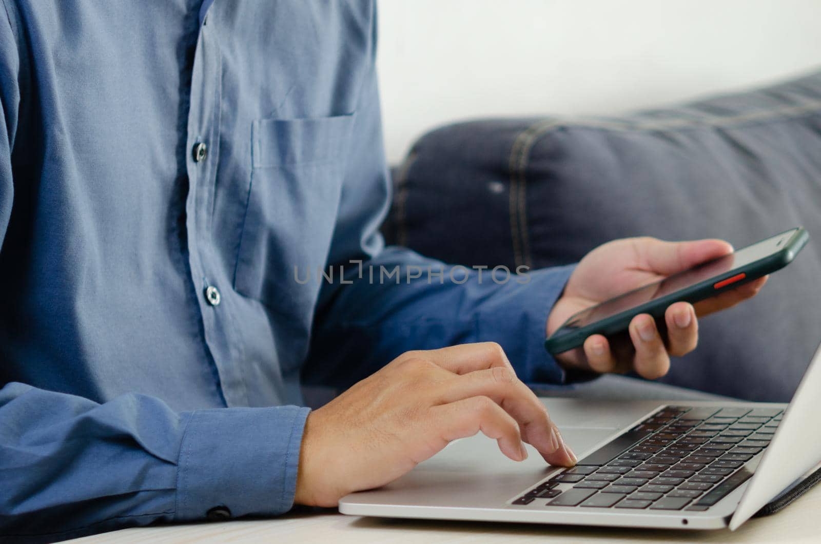 Businessman hand typing keyboard on laptop computer with smart phone. Close up businessman communicating internet and social media at his desk.