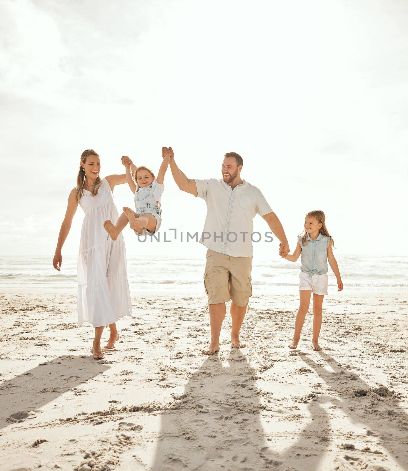 Carefree caucasian family walking and having fun together on the beach. Parents spending time with their daughters while on holiday. Little siblings holding hands with their parents on vacation by YuriArcurs