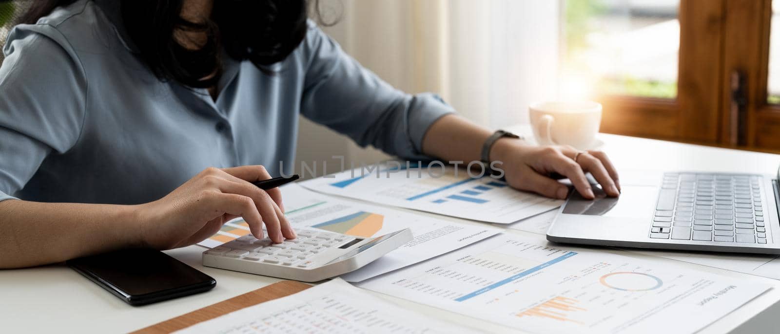 Close up young woman using calculator and laptop, checking domestic bills, sitting at table with financial documents, managing planning budget, accounting expenses, browsing internet service.