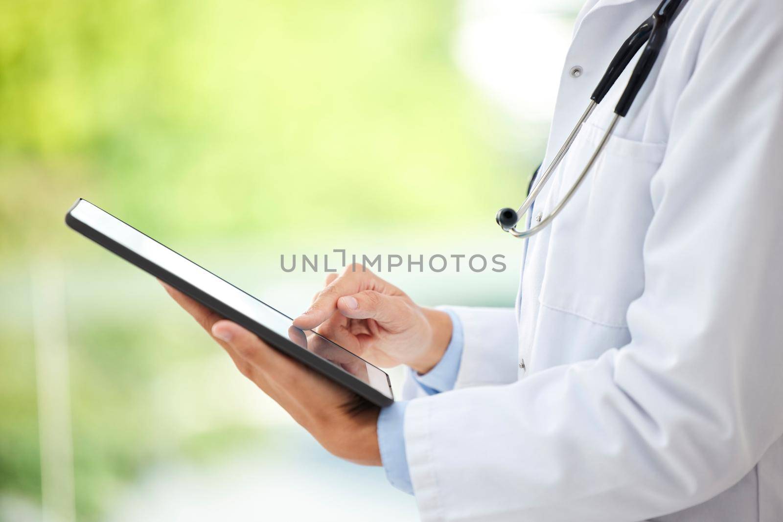 Closeup of female doctor working on her digital tablet in the office. A unknown mixed race and professional young woman working in a hospital office. Health resources are easy to find online by YuriArcurs