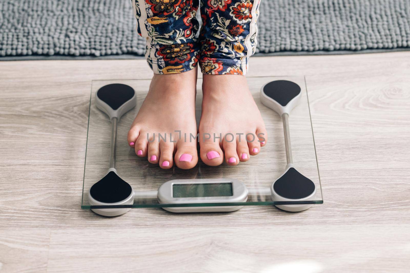 Legs of a girl standing on scale to measure weight. Caucasian female bare feet with weight scale at home. Person checking the weight on the scale. Dieting, control and measuring. by uflypro