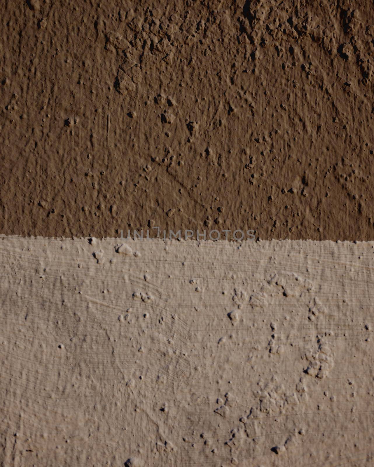 Close-up on a wall made of two-tone plaster. The wall is painted with dark brown and light brown paint.