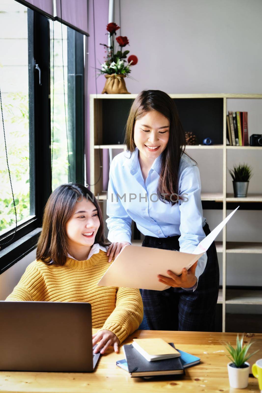 Two female company employees happily smiled at each other as they handed each other folders. by Manastrong