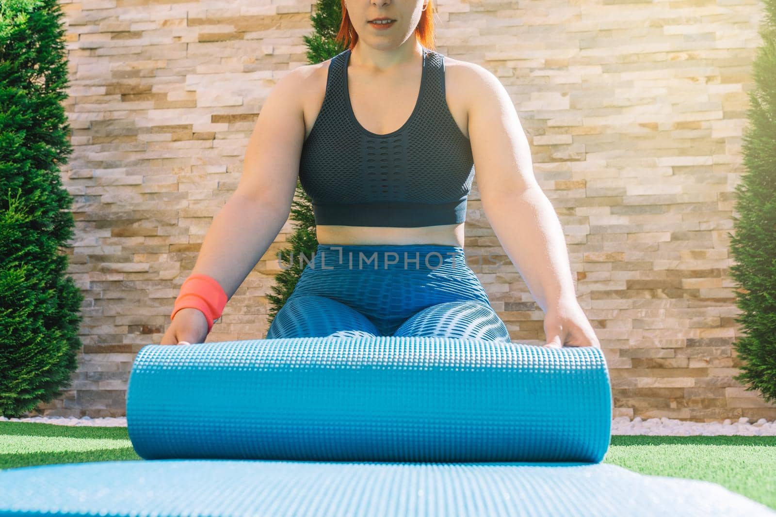 cropped shot of a young fitness woman, stretching a yoga mat to practice relaxation exercises. unrecognisable girl doing sports exercises at home. concept of health and wellness. by CatPhotography