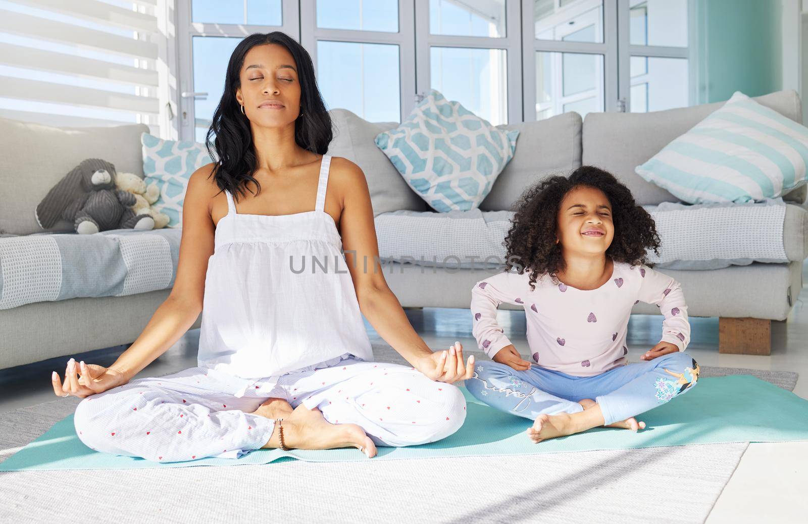 a young mother and daughter meditating together at home.