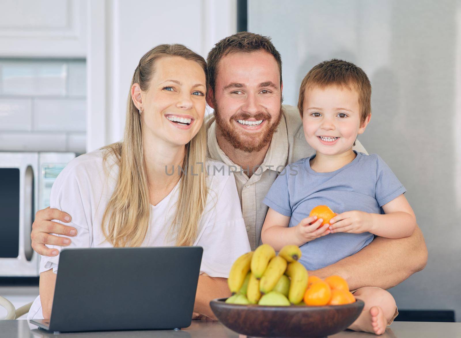 Happy family relaxing in the kitchen. Little boy eating orange in the kitchen. Cheerful caucasian family at home. Father hugging wife and son. Two parents bonding with their son. Young family laughin by YuriArcurs