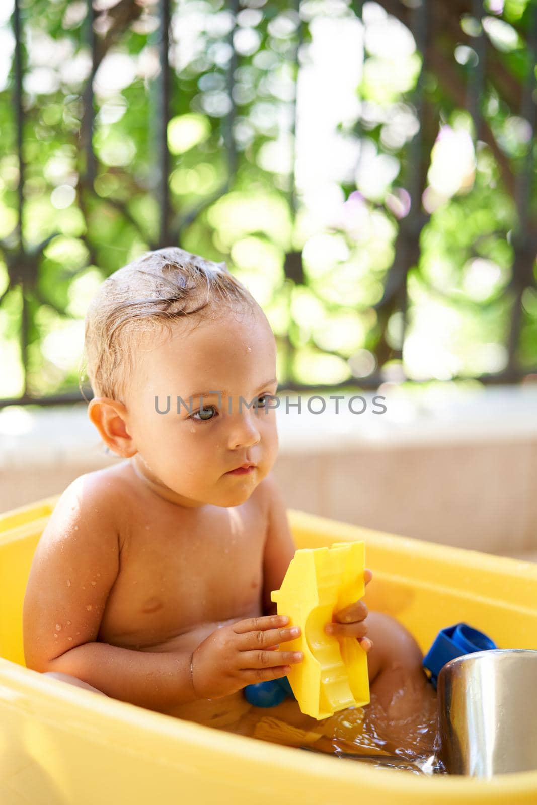 Little girl sits in a bowl of water with a toy in her hands by Nadtochiy