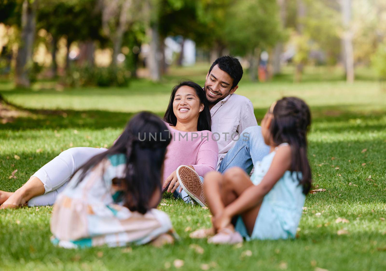 Portrait of happy asian couple lying together on grass. Kids playing while watching their loving parents spending time together at the park.