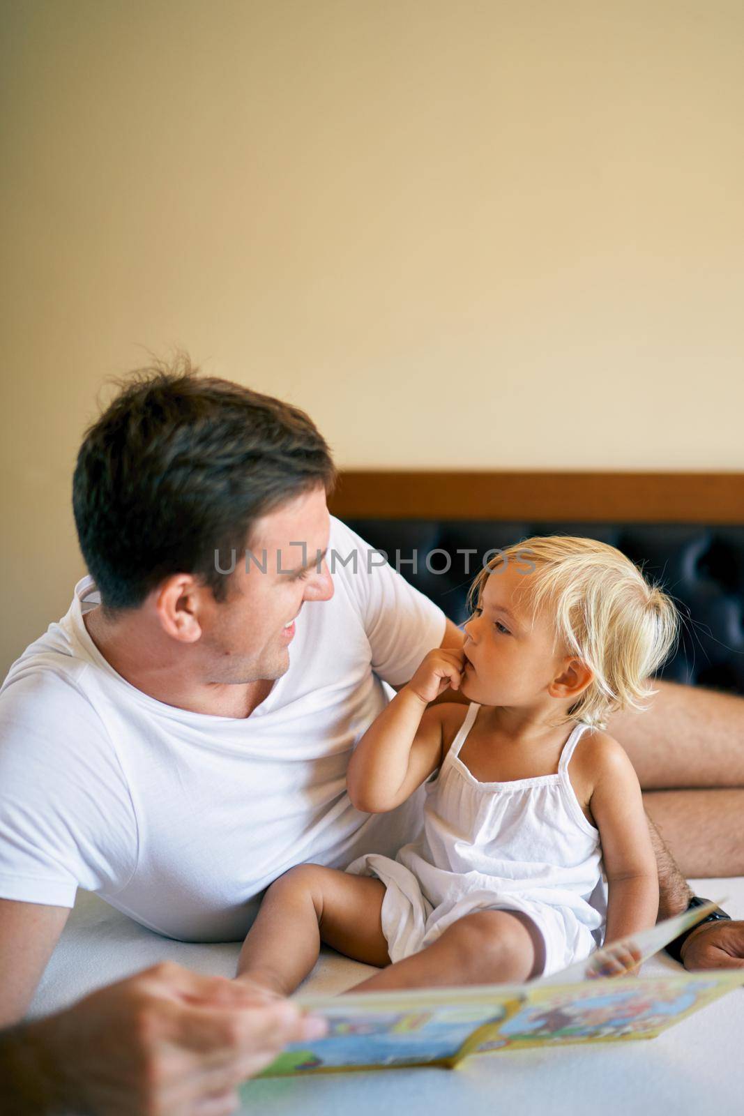 Smiling dad reading colorful book to little girl. High quality photo