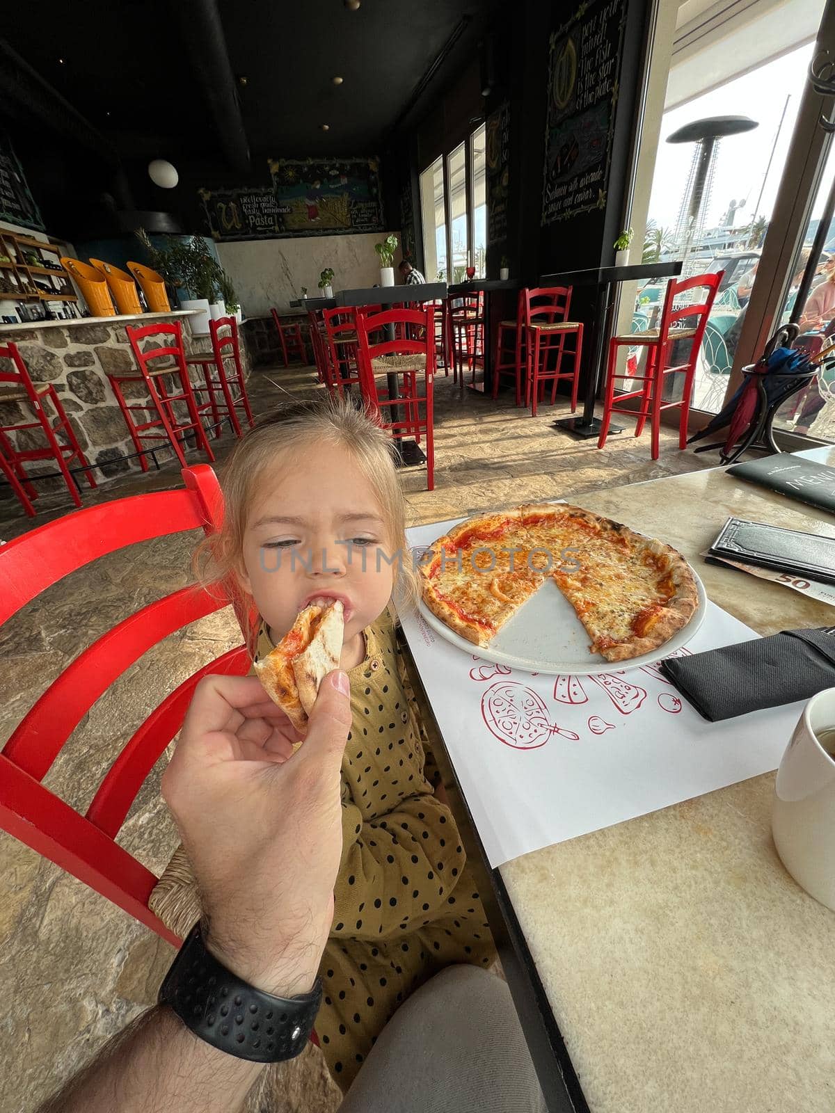 Dad feeding little girl with pizza in a restaurant. High quality photo
