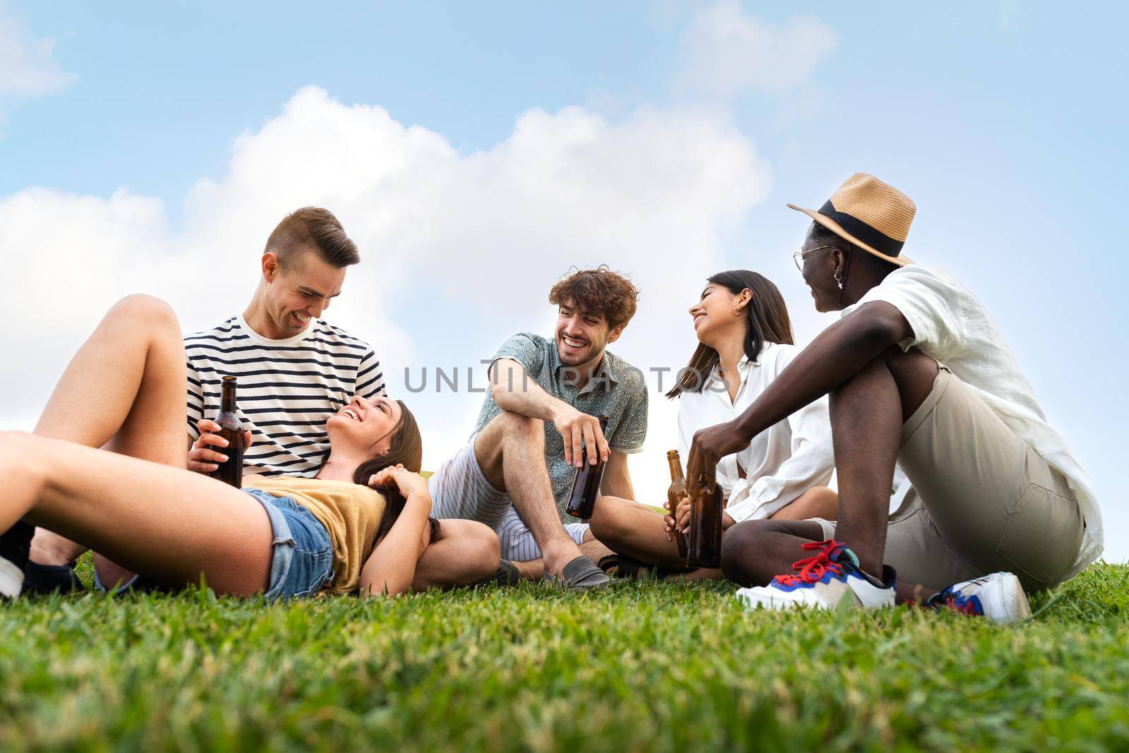 Diverse group of friends relaxing outdoors in nature, laughing, having fun, enjoying some beers together. by Hoverstock