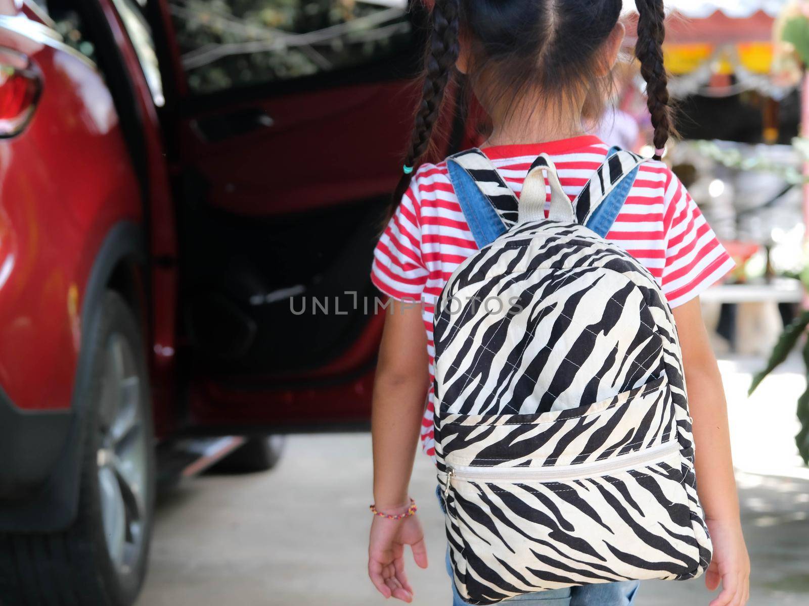 Rear view of happy smiling little girl with backpack getting in the car to ride to school. Little girl is happy and ready to learn. Back to school. by TEERASAK