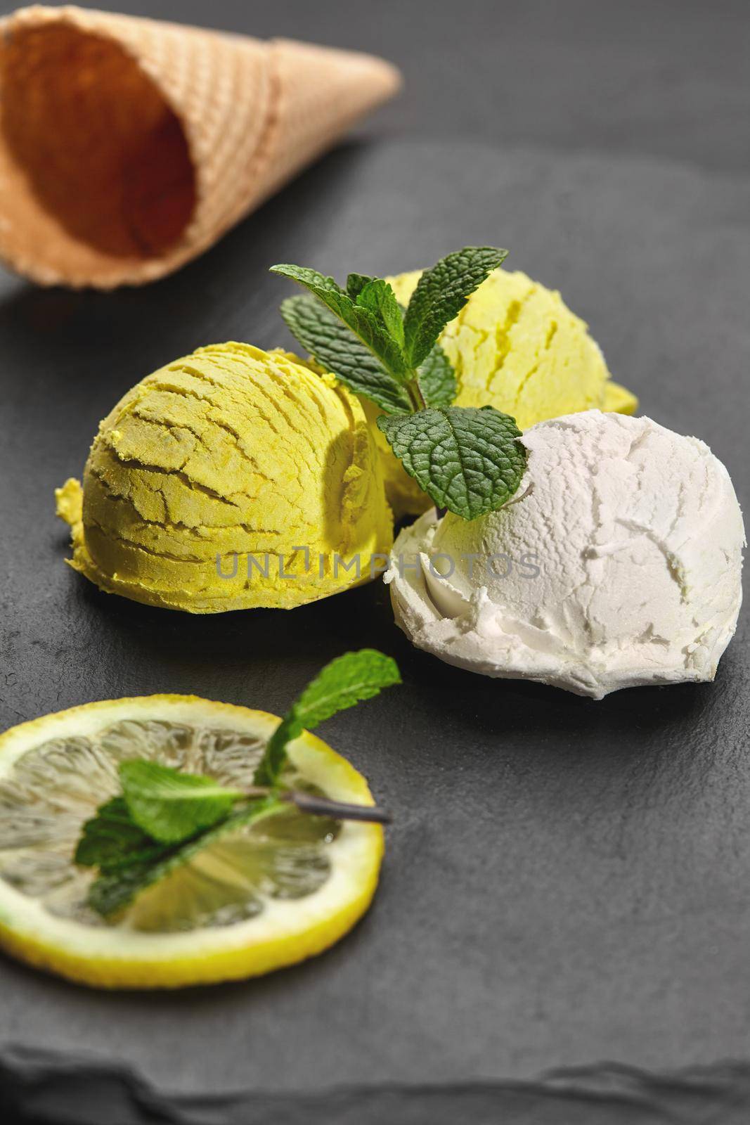 Close-up shot of a natural gourmet creamy and lemon ice cream decorated with fresh mint and served on a stone slate over a black background.