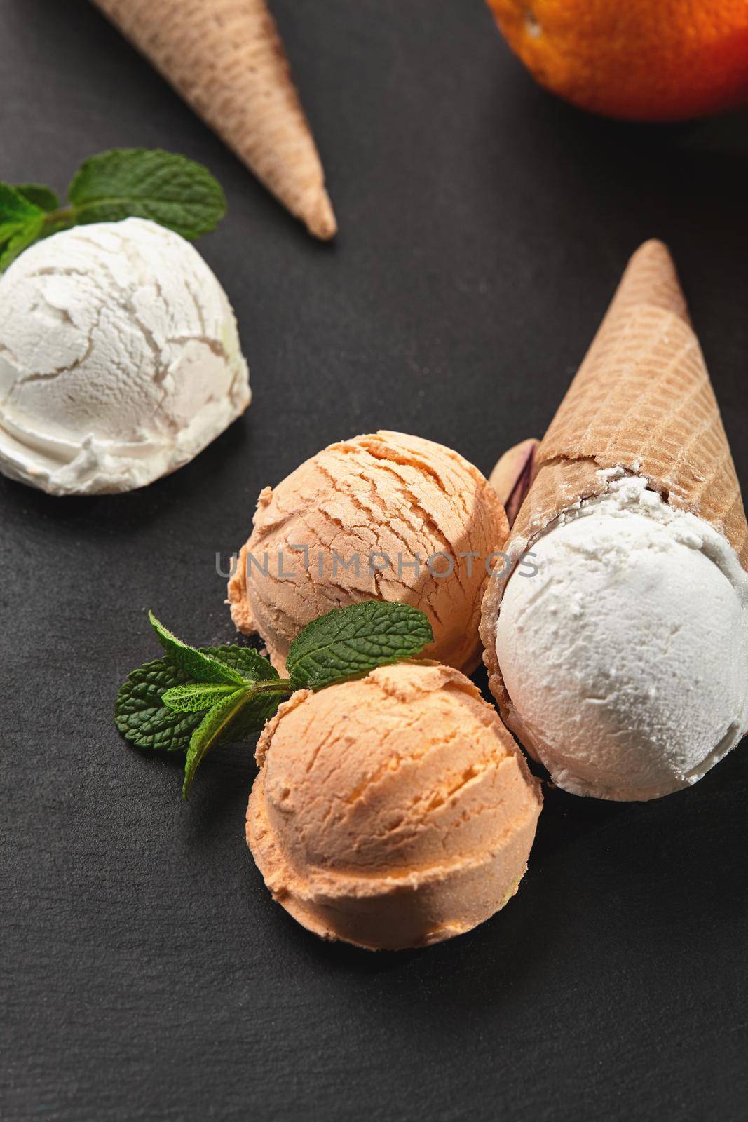 Close-up shot of a delightful creamy and orange ice cream decorated with fresh mint and classic waffle cones on a black background. Summer coolness of ice cream and sorbet.