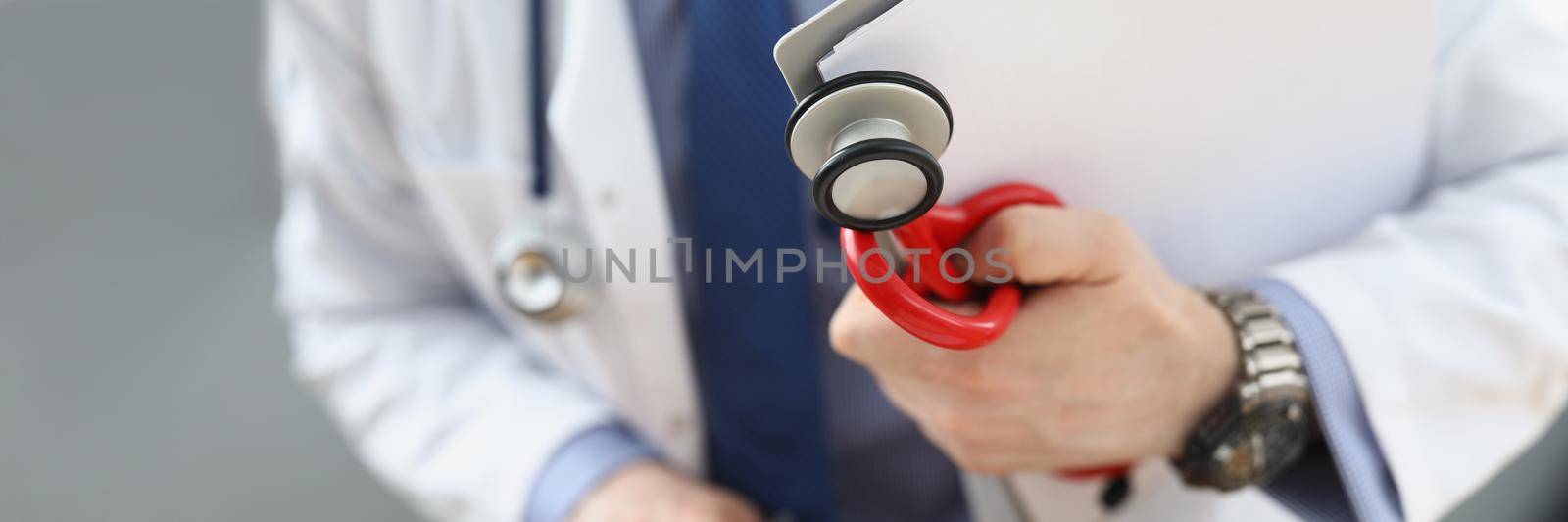 Close-up of doctor holding medical equipment red stethoscope and patient medical history. Medical building for health checkup. Medicine, clinic concept