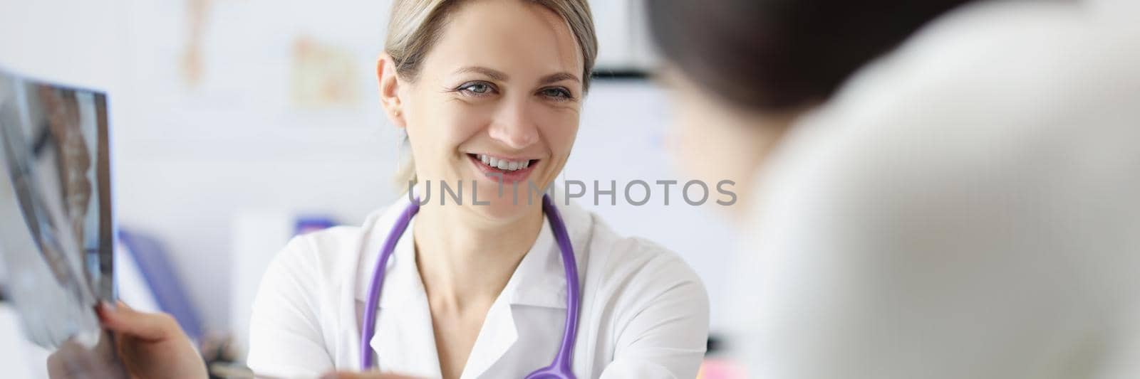 Portrait of female doctor show x ray result to patient and explain, professional specialist joking about disease. Medicine, healthcare, appointment concept