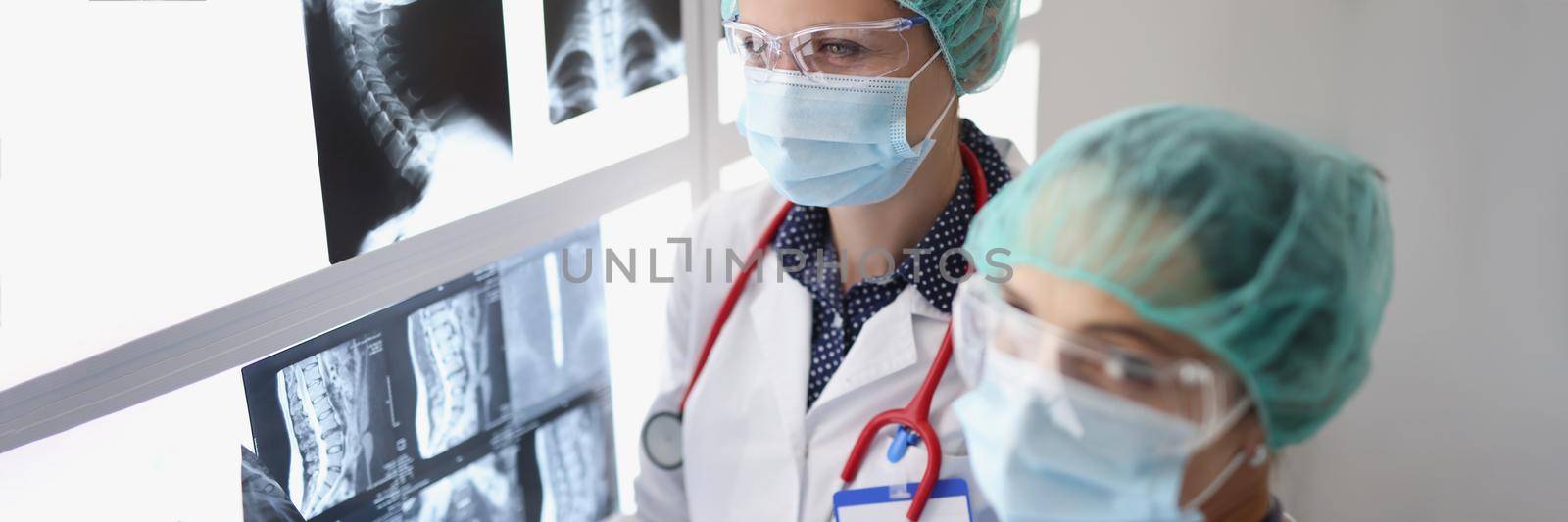 Portrait of women professional doctors look through x ray scans in hospital, examine patients result. Colleagues in protective uniform. Medicine concept