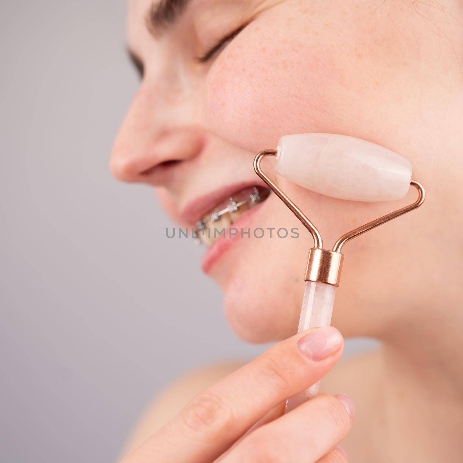 Close-up portrait of a woman uses a quartz roller massager to smooth wrinkles on her forehead. by mrwed54
