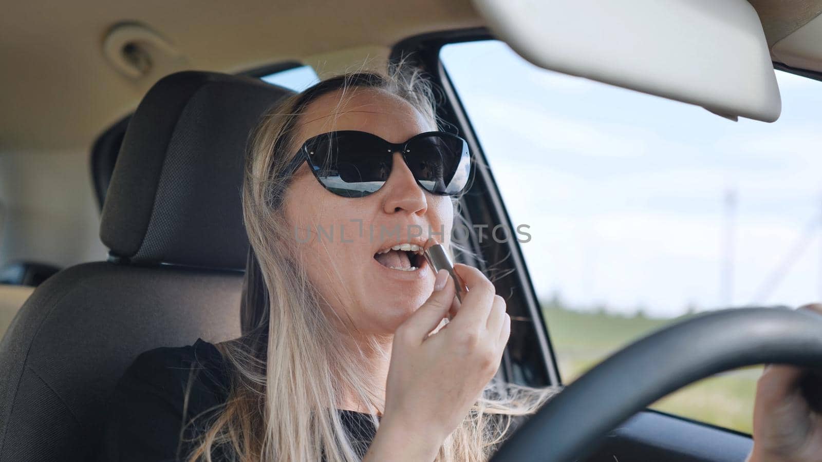 A woman paints her lips while driving