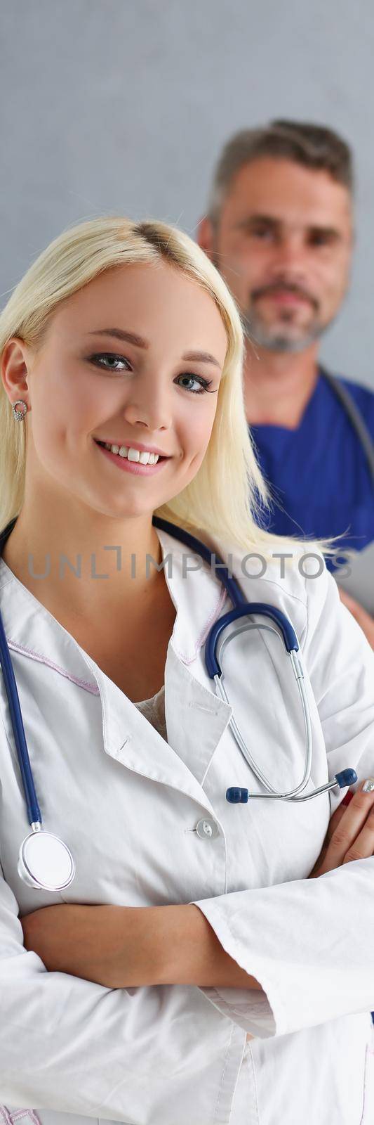 Portrait of young smiling woman start full working day in clinic after internship. Happy doctor in uniform, people support behind. Medicine, help concept