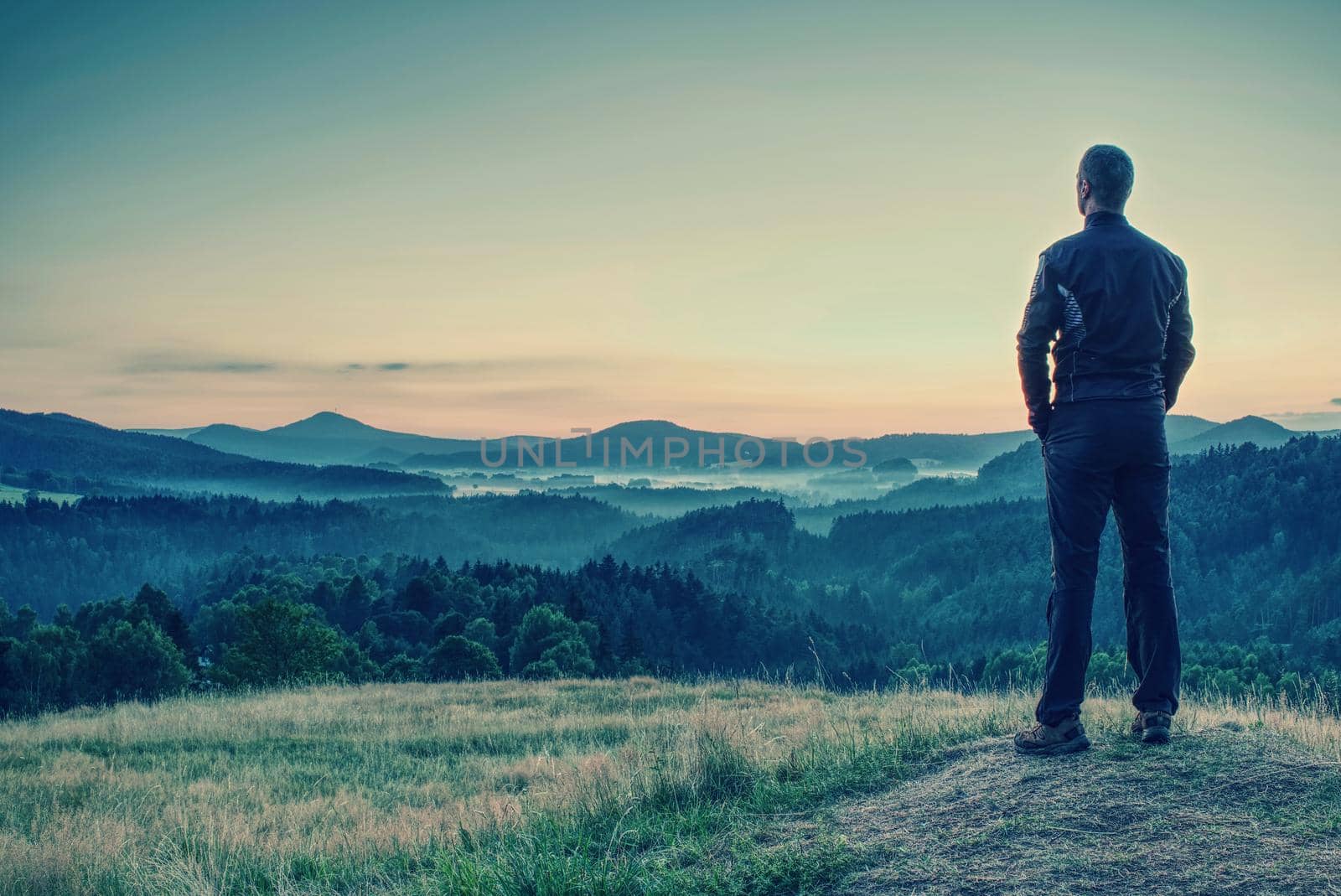 Man tourist traveler standing on cliff of mountain and looking to sunset, against backdrop of hills. Concept active recreation in mountains