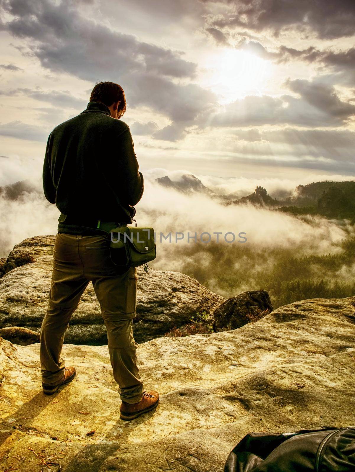 Photographer bend head check display of camera. Man stay on cliff and takes photos. Autumn beautiful misty landscape misty sunrise at horizon