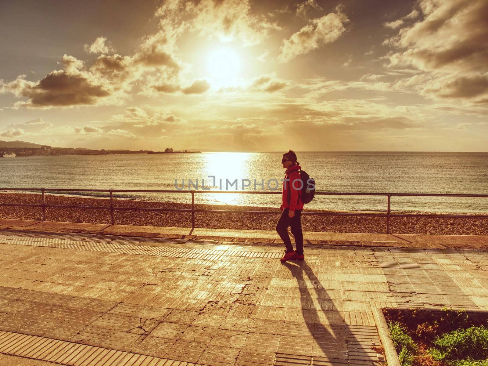 Female backpacker walk or strolling along the beach promenade, sun at horizon