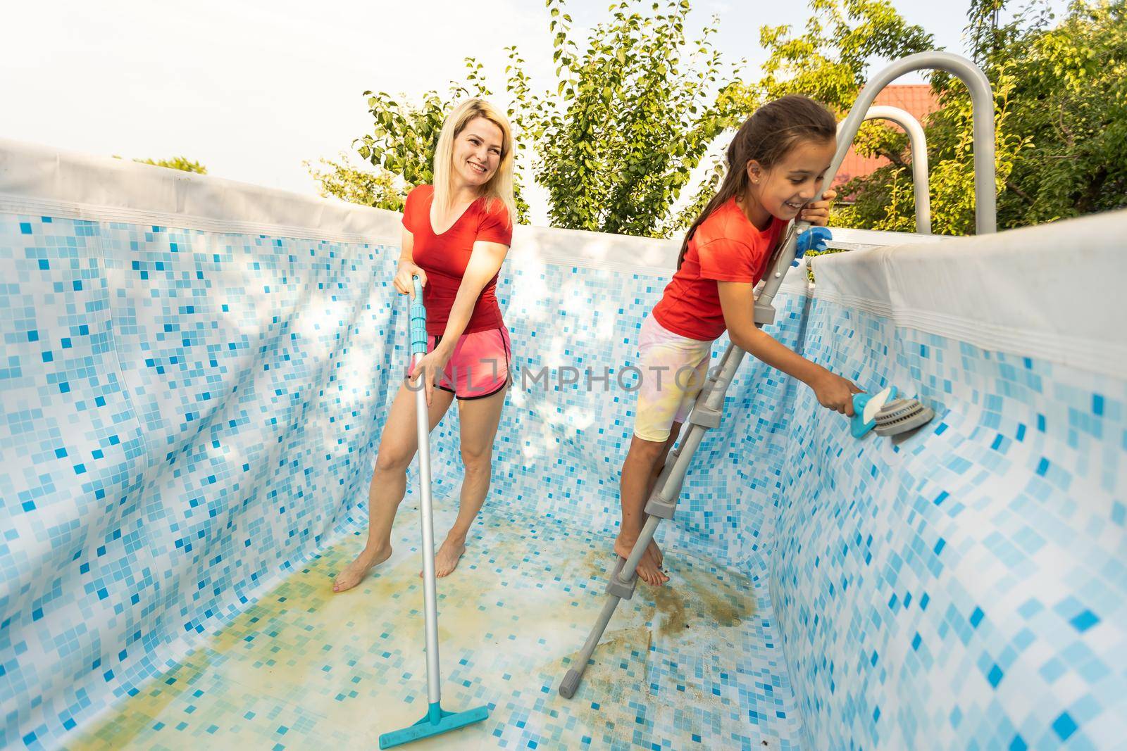 mother and daughter cleaning swimming pool in the garden. by Andelov13
