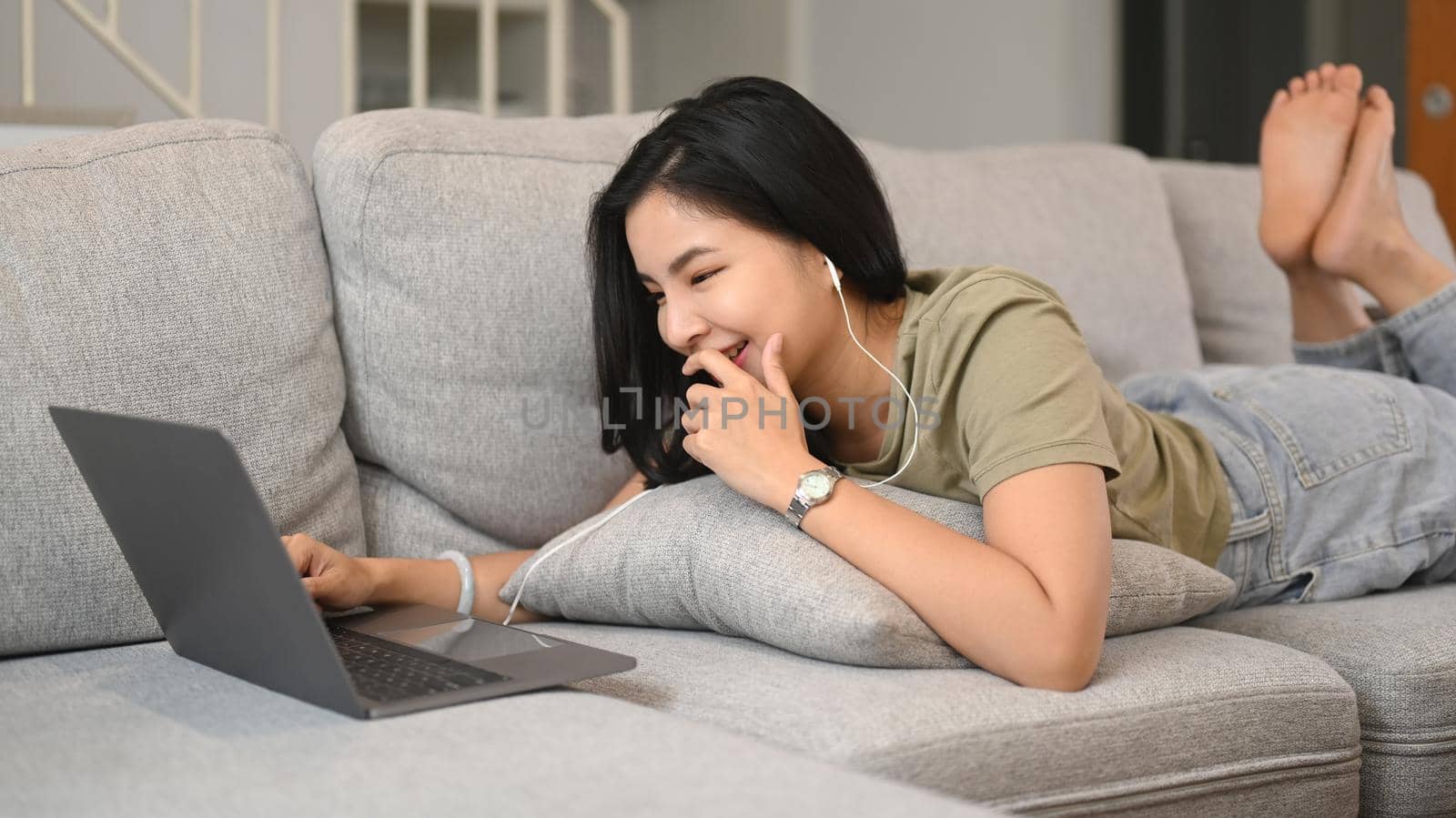 Pretty young asian woman in casual clothes lying on sofa and video call on laptop computer.