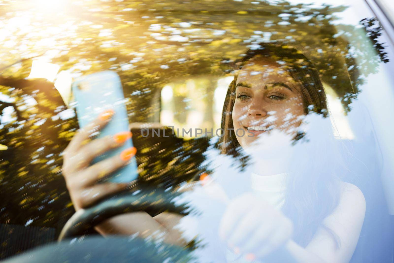 Attractive young student girl in casual clothes using mobile phone, sending messages while driving a car by VitaliiPetrushenko