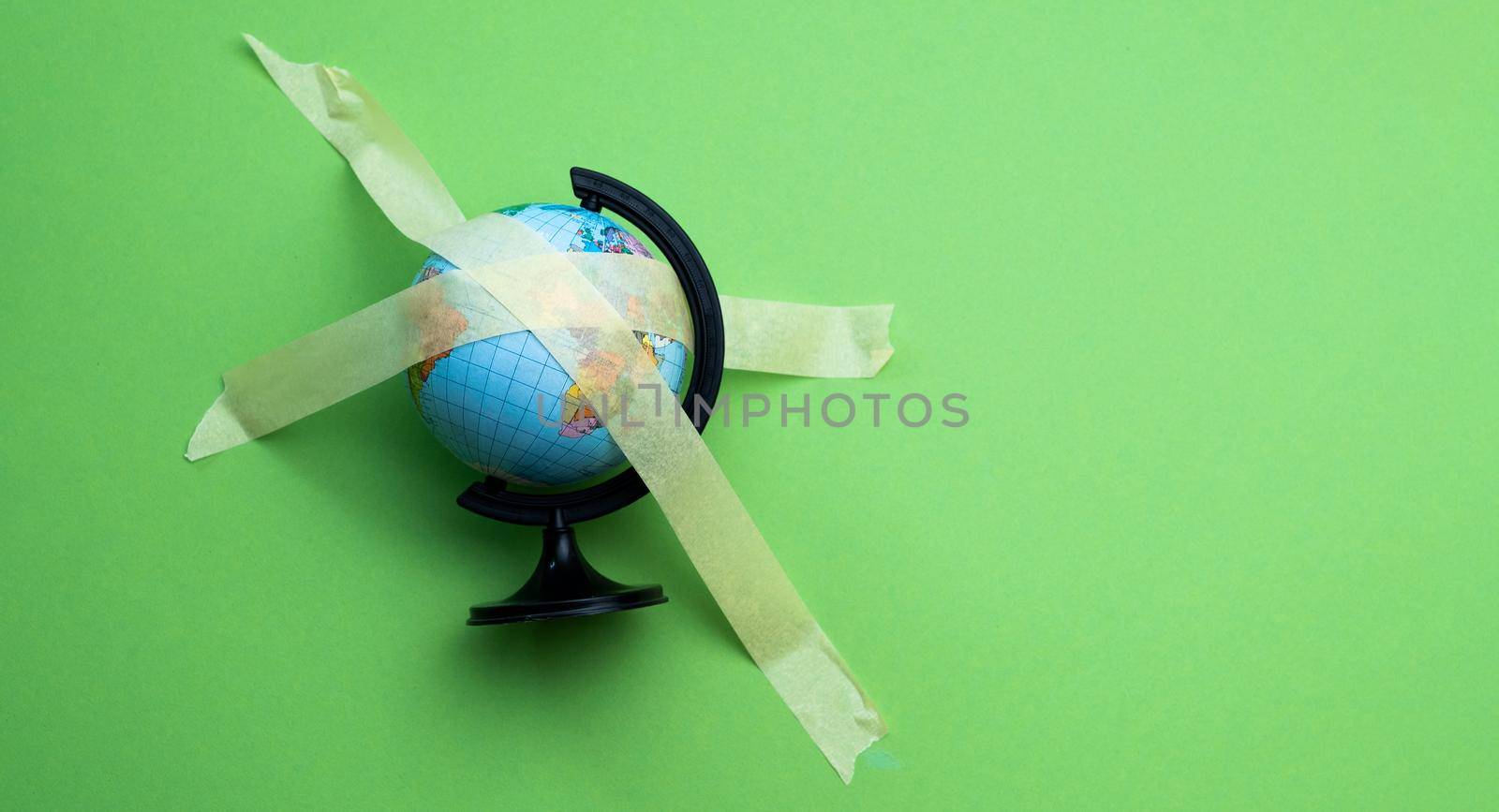 The globe sticked up with masking tape isolated on green background wit copyspace. World epidemic concept with stopped tourism and travel. Abstract symbol of closed country borders for travellers