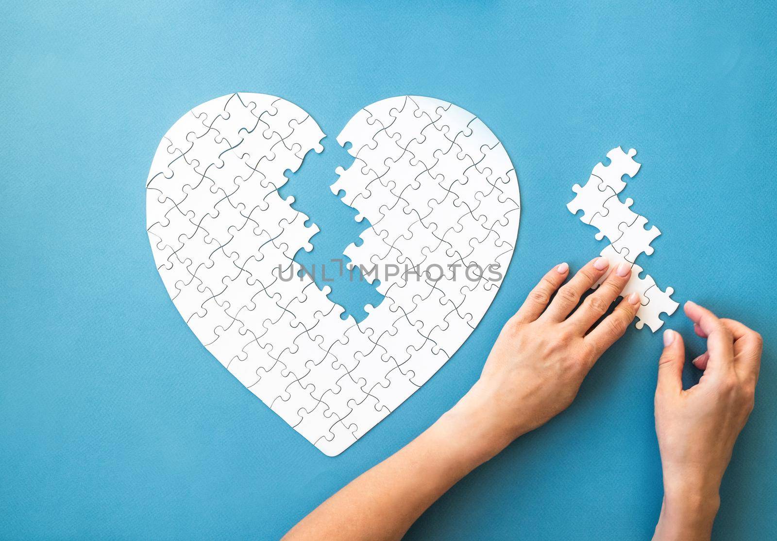 White puzzle in heart shape. White details of puzzle in hands on blue background.