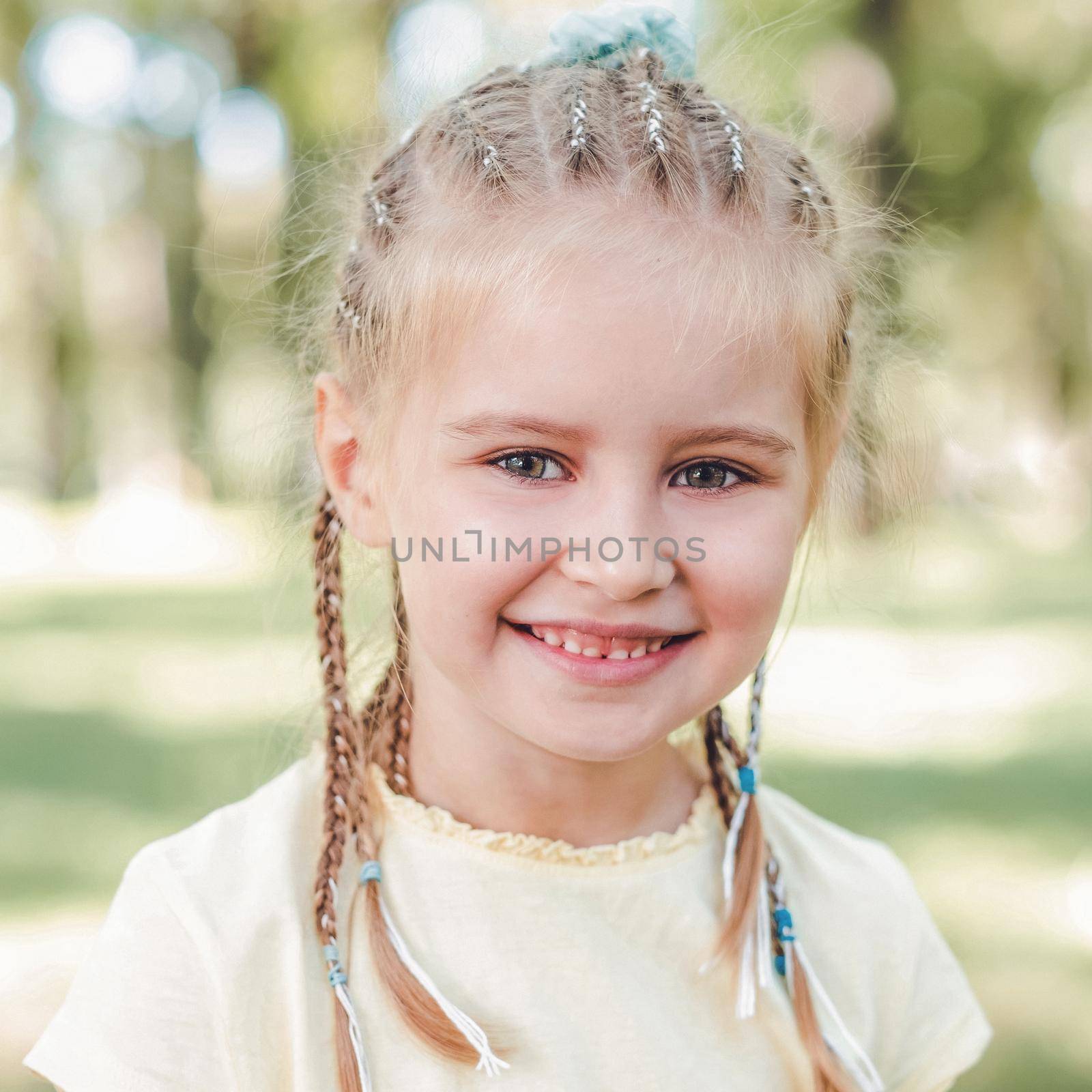 Closeup portrait of beautiful blond girl with cute hairstyle with blurred nature background