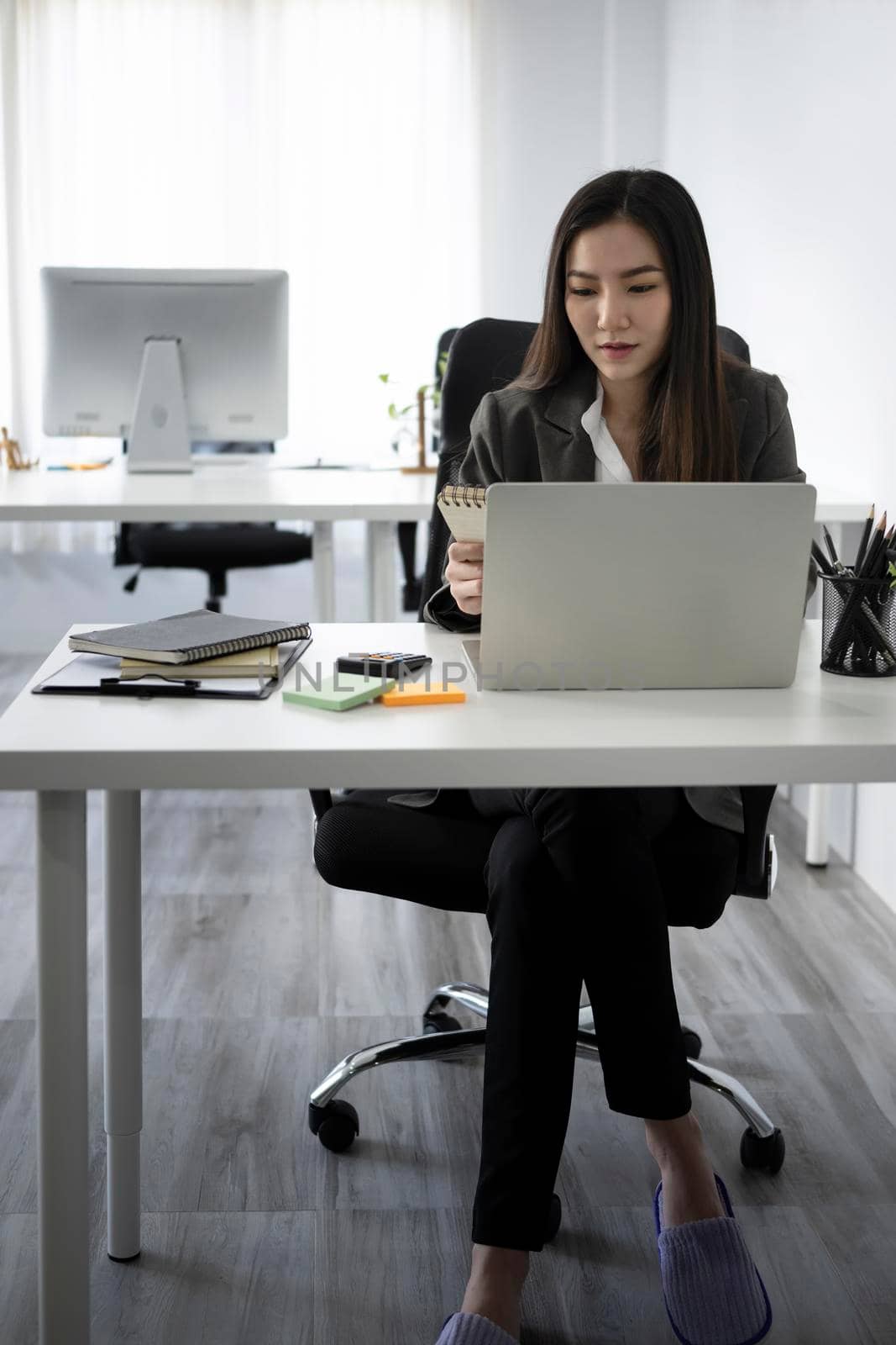 Full length portrait of beautiful businesswoman sitting at office desk and using laptop computer.