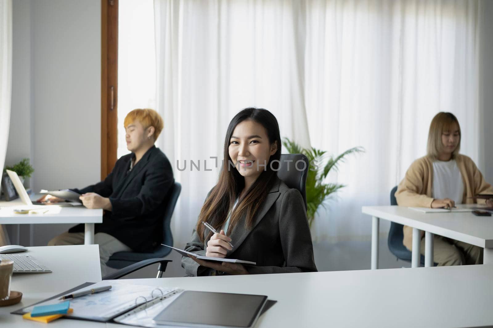 Confident businesswoman sitting with her colleagues in office and smiling to camera.