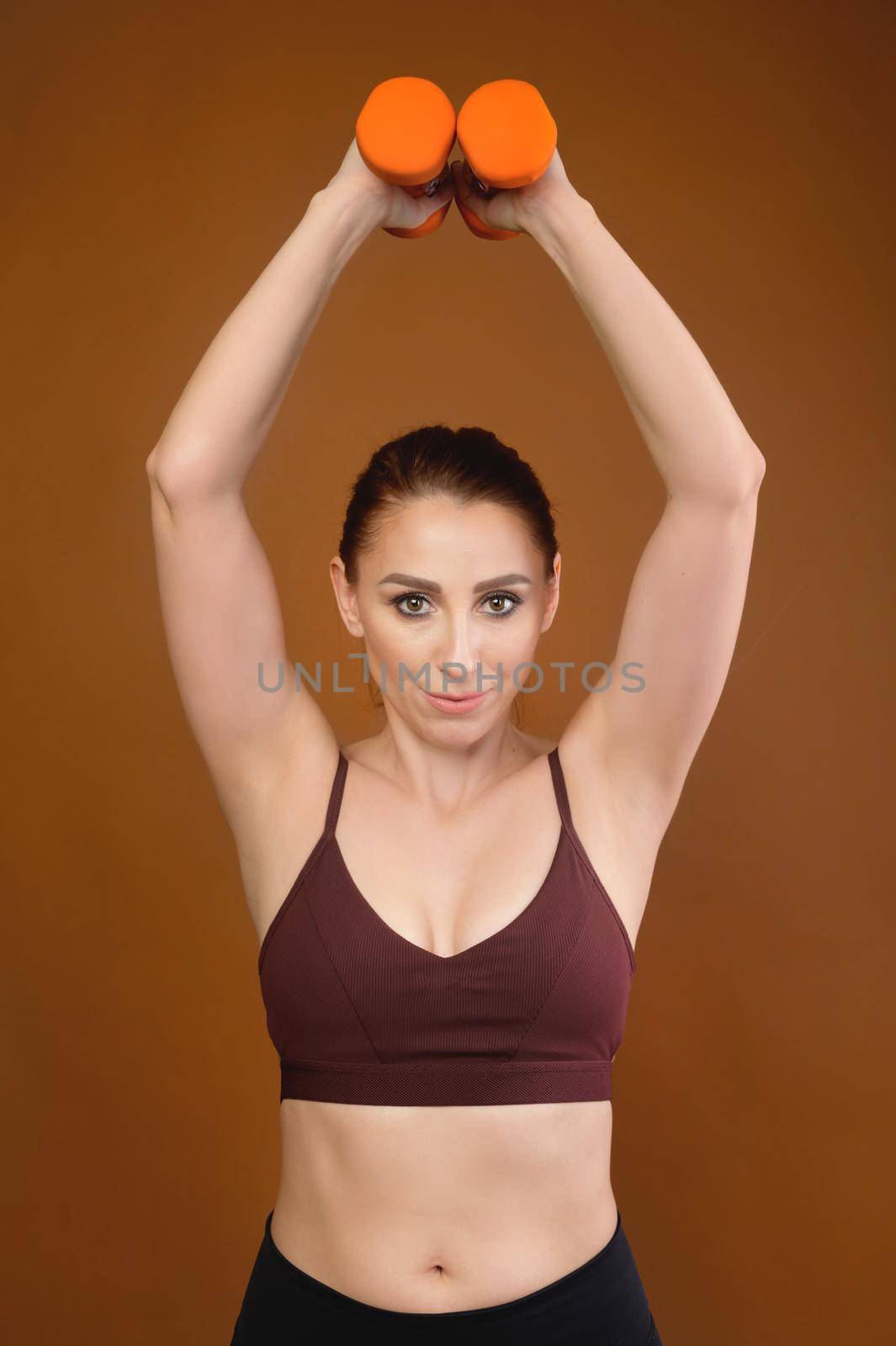 Portrait of a slim athletic woman doing exercises with small dumbbells, studio shot by yanik88