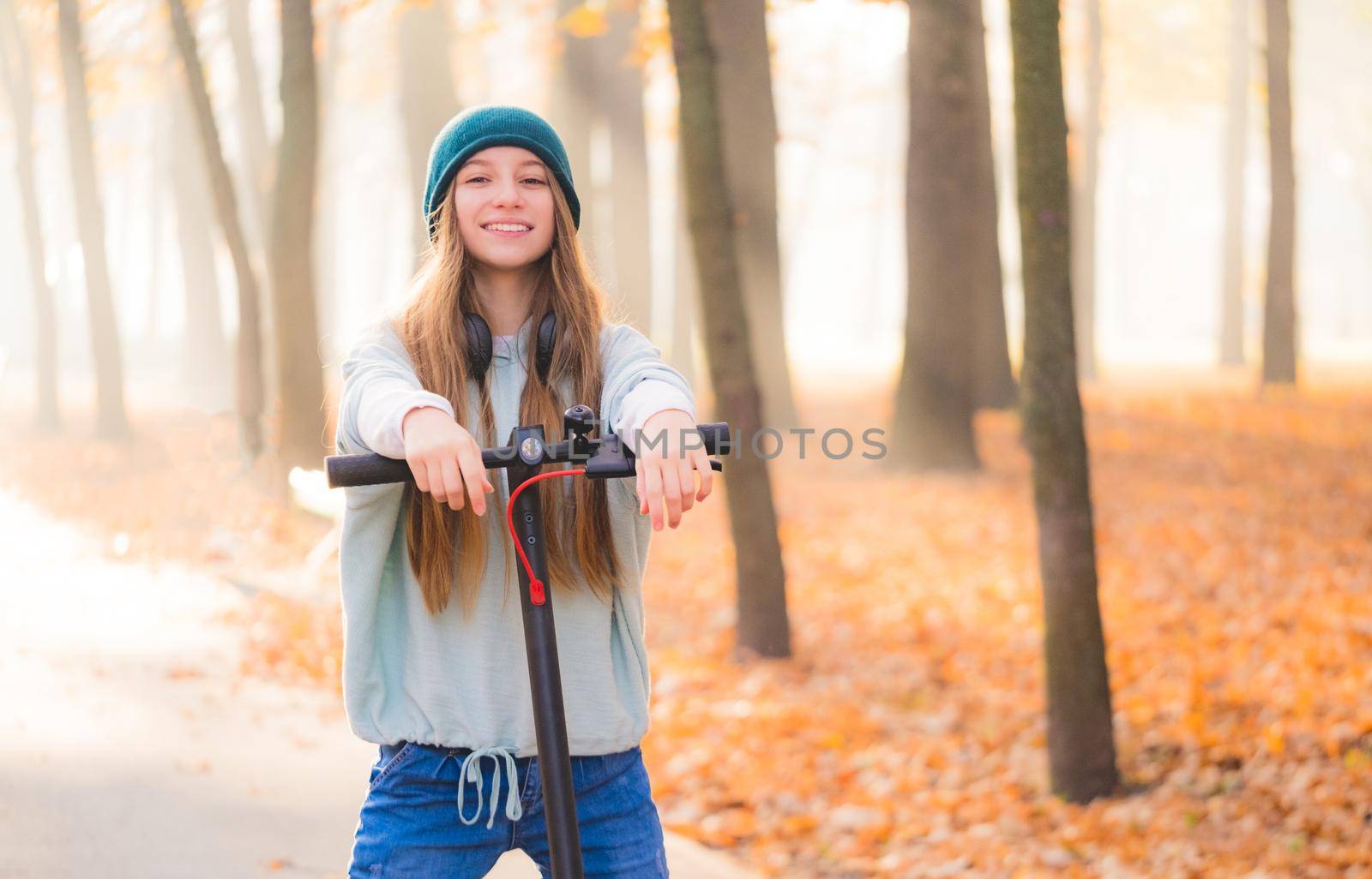 Lovely teenage girl with scooter resting in autumn park