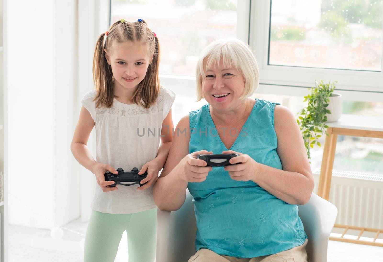 Happy aged woman playing video game with granddaughter