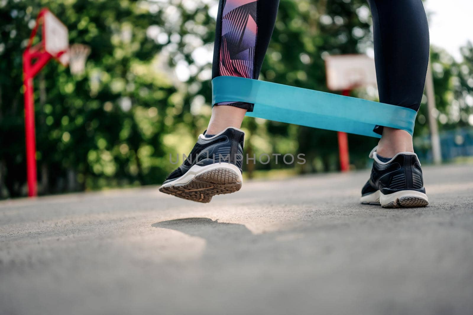 Young girl woman exercising outdoors with mini rubber elastic band doing workout. Closeup view of female person legs during active training with additional sport equipment outside