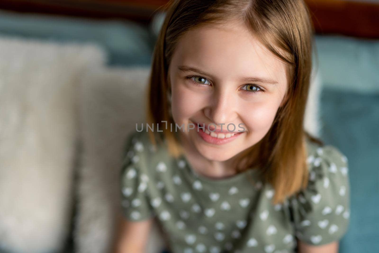 Closeup portrait og cute preteen kid girl looking at the camera and smiling. Little schoolgirl model with pretty face in the bedroom