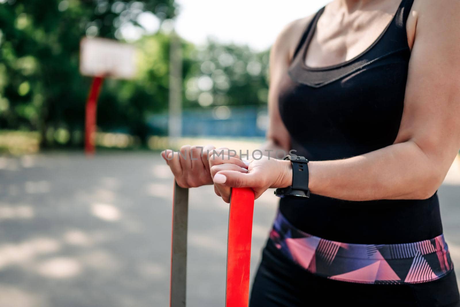 Young girl woman exercising outdoors with rubber elastic band doing training for her hands. Closeup view of active fitness with additional sport equipment outside