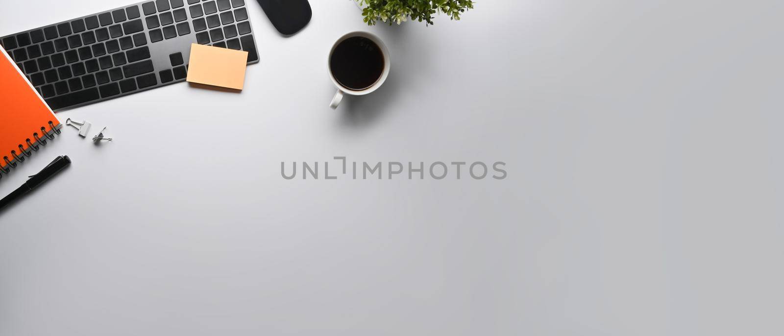 Flat lay wireless keyboard, coffee cup, notebook and potted plant on white table.