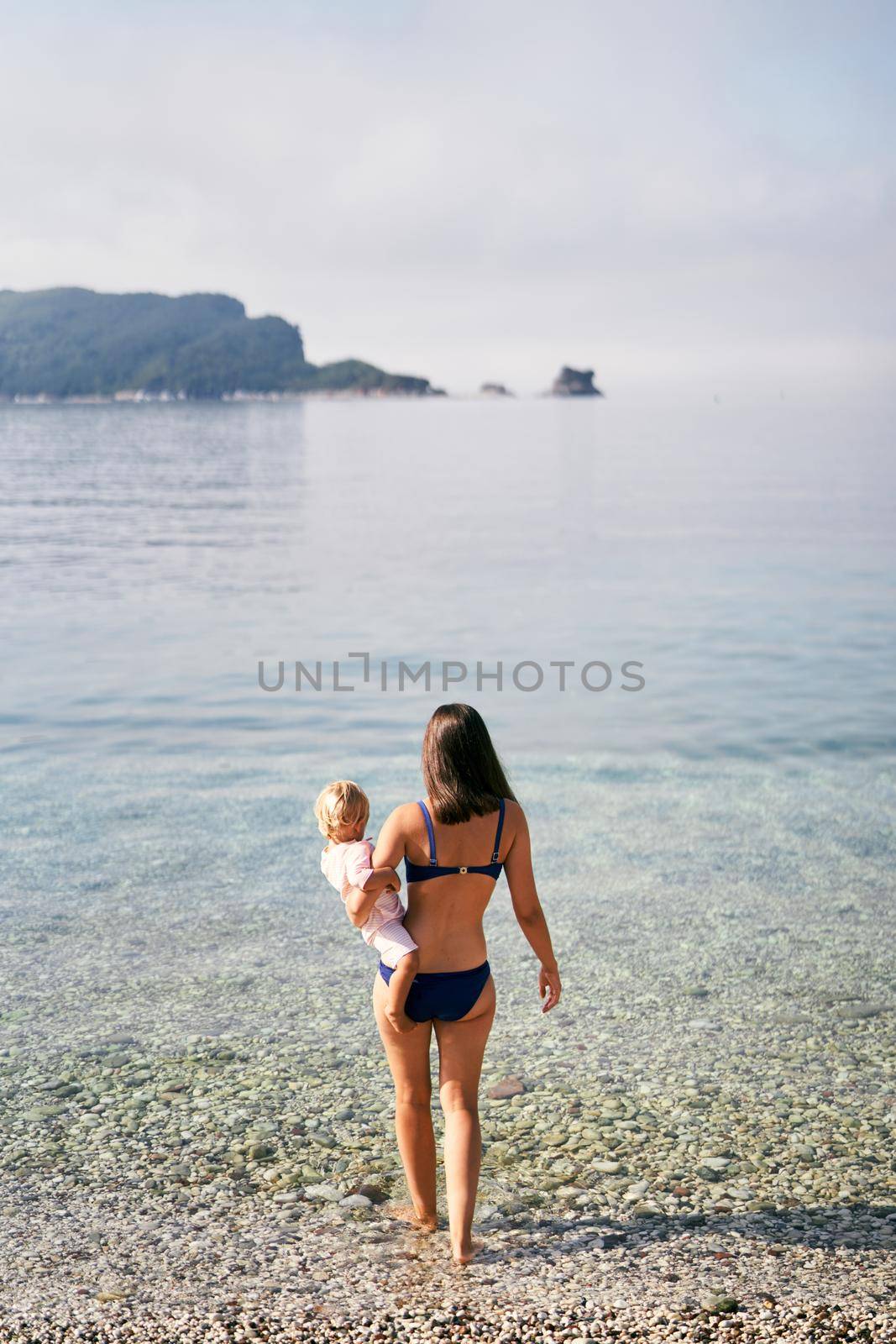Mom with a little girl in her arms walks along the seashore. High quality photo