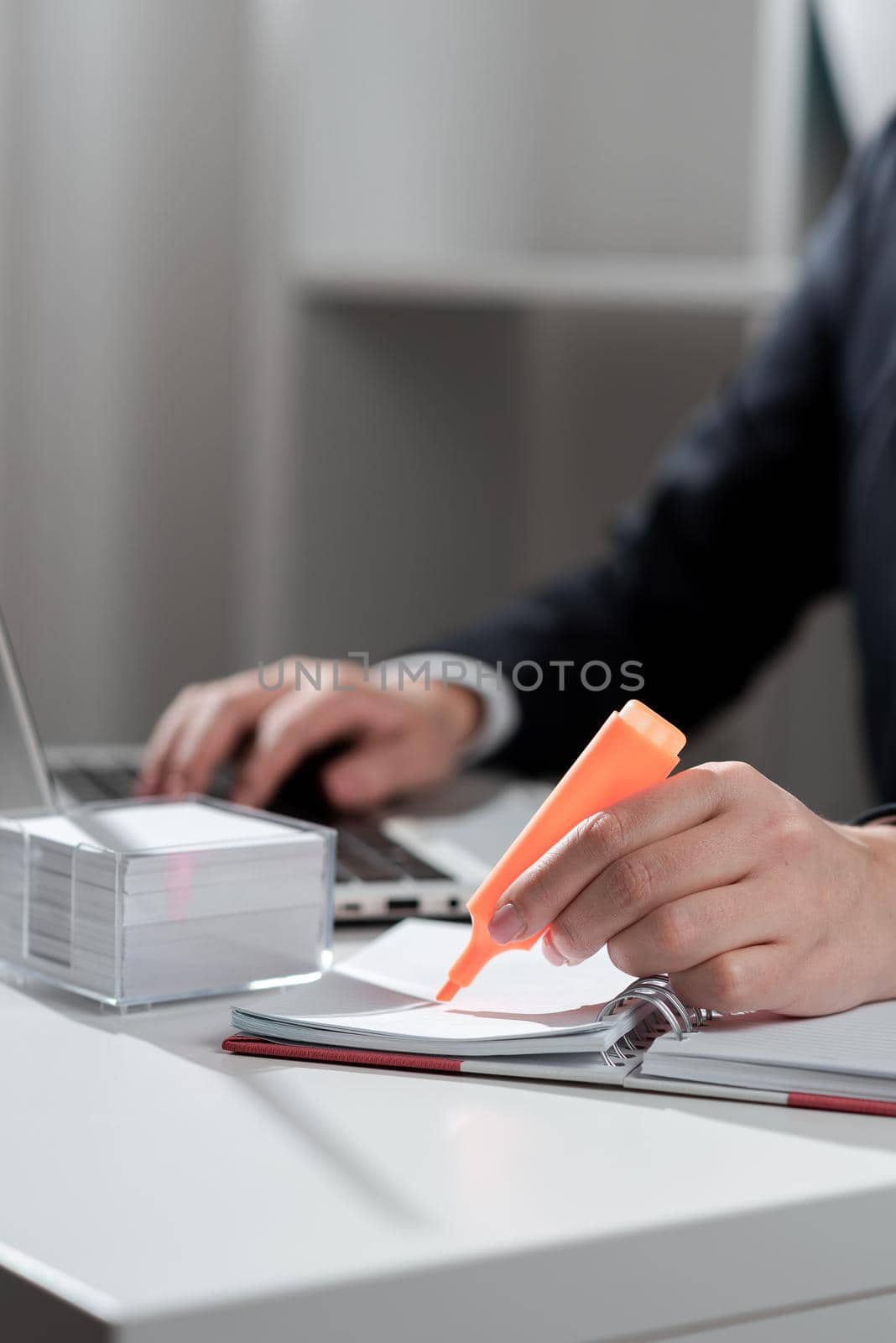 Businesswoman Writing In Notebook And Typing On Lap Top On Desk With Notes. Woman In Suit Holding Marker And Doing Work On Computer On Table With Memos. by nialowwa