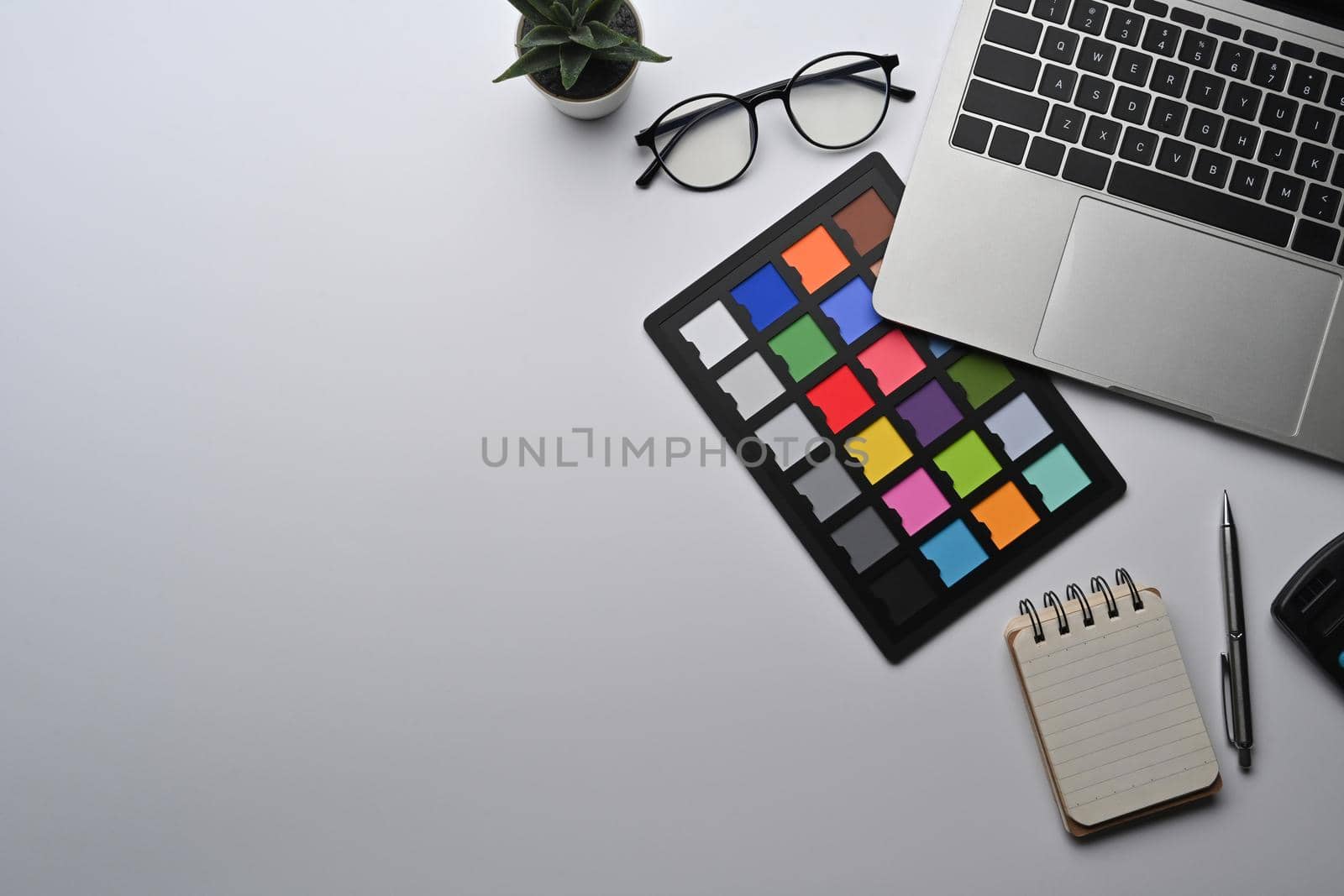Creative designer workspace with laptop computer, notebook, glasses and color swatch.