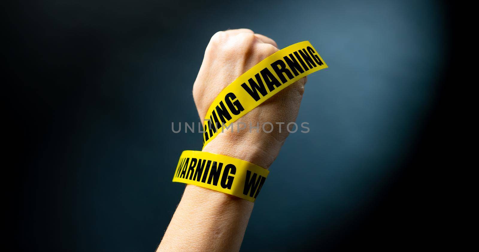 Hand wrapped with yellow caution tape with warning words. Concept of forbidden actions and power